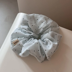Detailed view of light blue polka dot scrunchie with sheer texture and brand label