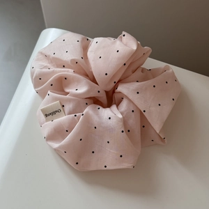 Detailed close-up of light pink hair scrunchie with black polka dots and woven brand label