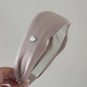 Détail d'un bandeau en maille rose poudré avec pendentif coeur argenté et doublure en tissu