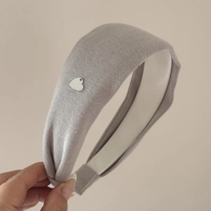 Détail du serre-tête tricoté gris orné d'un petit pendentif en forme de cœur argenté