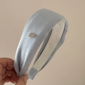 Détail d'un serre-tête en tricot bleu clair avec un pendentif en métal argenté en cœur
