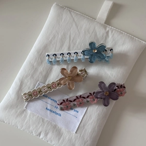 Détails de barrettes brodées avec fleurs en résine et strass sur fond blanc doux