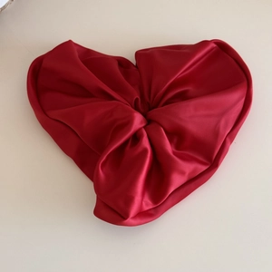 Macro shot of a red heart-shaped satin scrunchie with smooth texture and glossy silk finish