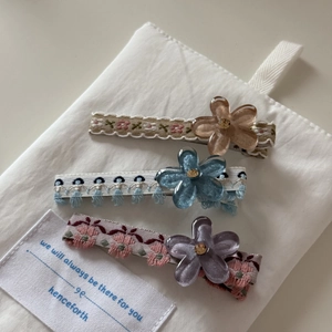 Vue détaillée de trois barrettes à fleurs brodées avec strass et pétales en acrylique pur