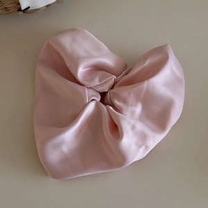 Macro shot of a soft pink satin scrunchie arranged in a heart shape on a beige base
