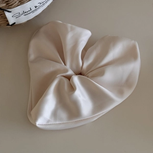 Detailed texture of a soft beige satin scrunchie with elegant silk folds and smooth luster