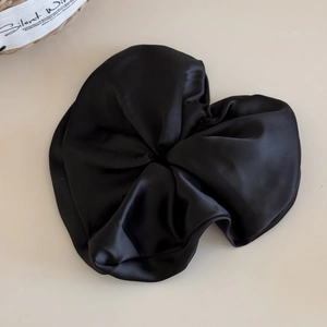 Macro detail of glossy black satin scrunchie with smooth silk texture and soft folds