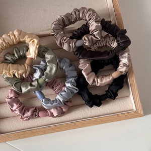 Elegantes Set aus bunten Satin-Haargummis in beige Schmuckschale mit seidiger Textur