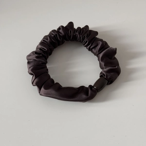 Detail eines dunklen Satin-Haargummis mit Glanzoptik und dekorativer ovaler Perle