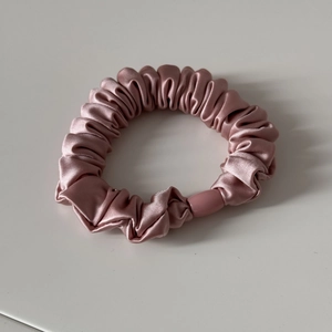 Detailansicht eines rosa Satin-Haargummis mit glatter Seidenstruktur und Kunststoff-Schnalle