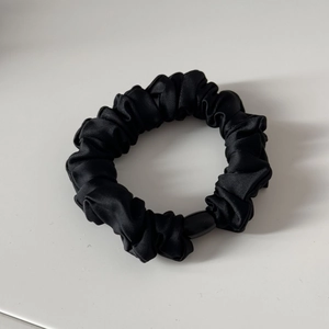 Detail eines schwarzen Satin-Scrunchies mit Falten und poliertem Harz-Verbindungsteil