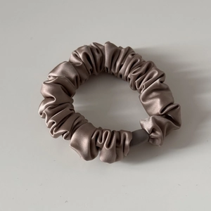 Detail eines champagnerfarbenen Satin-Scrunchies mit Seidentextur und Elastikband