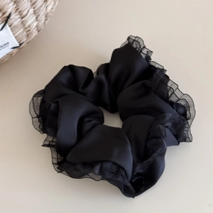 Close-up of black ruffled satin scrunchie with lace trim edge for elegant hair styling