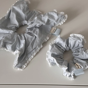 Pair of light blue fabric hair scrunchies with white lace edges and handmade labels