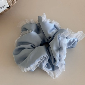 Close-up of light blue satin scrunchie with layered white lace ruffled edges