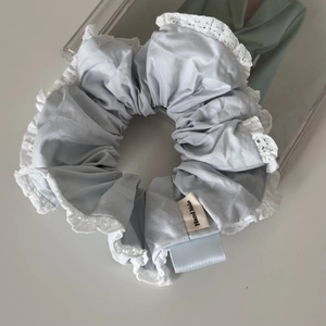 Detail of light blue fabric scrunchie with white lace edges and a Hand Made label