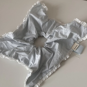 Detail of light blue handmade scrunchie featuring delicate white lace trim and textile tag