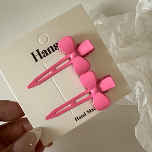 Détail de deux barrettes à cheveux nœud rose vif en métal sur une carte de présentation