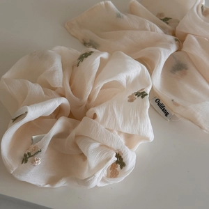 Gros plan détaillé de la broderie florale beige sur chouchou en tissu avec étiquette