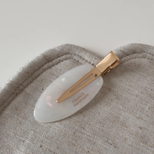 Macro detail of white marble acetate hair clip with gold logo on beige linen fabric