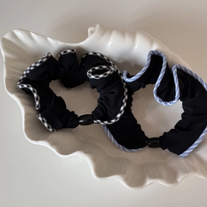 Chouchous en tissu noir avec bords à motifs et perle présentés dans un plat en coquillage