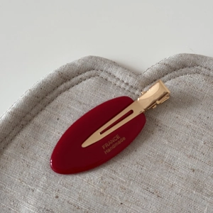 Macro detail of red acetate oval hair clip with gold France Handmade lettering