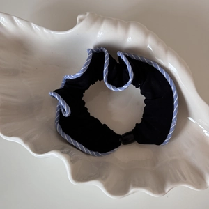Détail du chouchou en tissu noir avec bords à volants rayés bleus sur assiette blanche