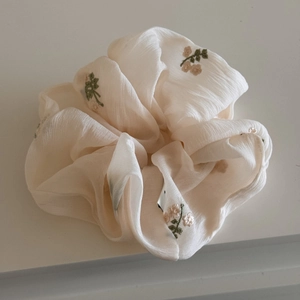 Détail d'un chouchou floral brodé en mousseline beige avec texture plissée douce