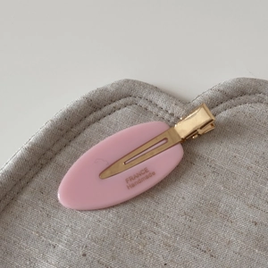 Detail showing the pink acetate oval hair clip with gold metal duckbill clip and handmade logo