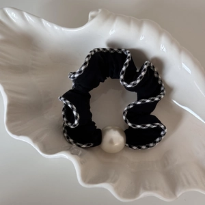 Détail d'un chouchou noir avec bordure vichy et perle sur un plateau en coquillage