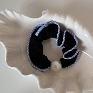 Détail d'un chouchou noir en tissu avec bordure rayée et une grande perle blanche