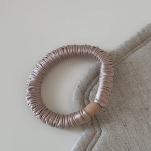 Détail d'un chouchou en satin champagne avec perle mate sur un tissu en lin naturel