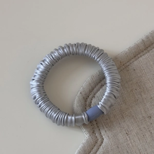 Détail d'un chouchou en satin gris argenté avec plis doux et attache en plastique bleue