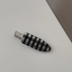 Close-up of minimalist silver hair clip with a classic black and white plaid pattern surface