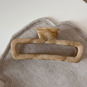 Macro detail of apricot marble pattern hair claw clip on neutral textured fabric pad