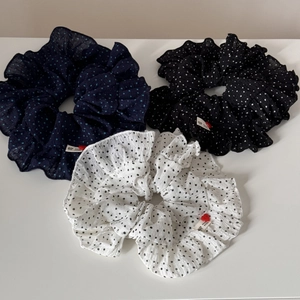 Detail of three polka dot ruffled scrunchies in navy, black, and white with handmade labels