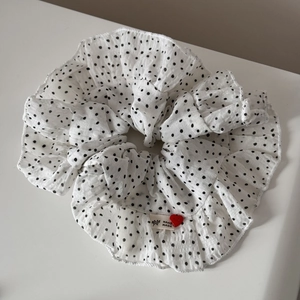 Detail of white polka dot scrunchie with ruffled edges and a handmade heart label