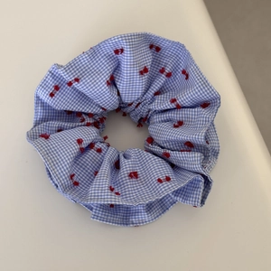 Detailed shot of blue and white plaid scrunchie with red bow embroidery and ruffles
