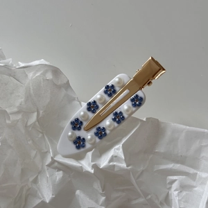 Detail of a white acetate hair clip with blue rhinestone flowers and faux pearls