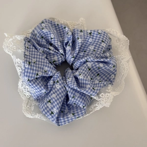 Detailed close-up of blue plaid scrunchie with white floral print and lace edge