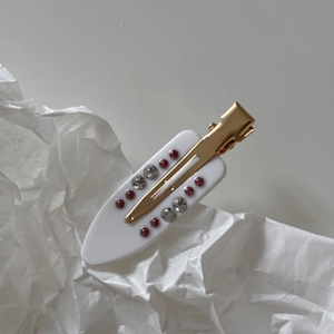 Detail of white acetate hair clip with gold metal base and sparkling crystal rhinestones