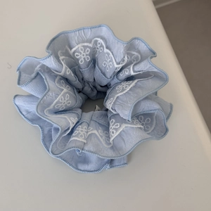 Close-up of light blue fabric scrunchie featuring delicate white lace floral embroidery