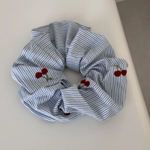 Detail view of blue striped scrunchie with red cherry embroidery and pastoral style texture