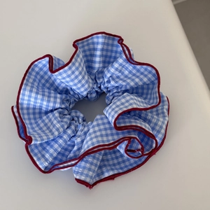 Detailed view of blue and white plaid scrunchie with elegant red stitching and pleats