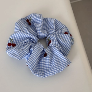 Detail of blue gingham scrunchie with red cherry embroidery and elastic texture