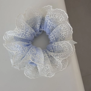 Detailed close-up of light blue fabric scrunchie with delicate white lace embroidery edges
