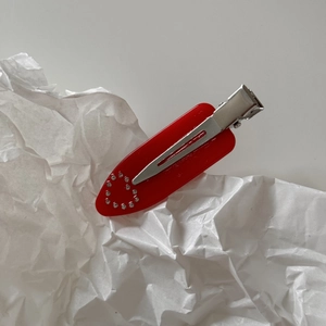 Detail of red marble texture hair clip with sparkling rhinestone heart on white paper
