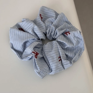 Detail of blue striped scrunchie with red bow embroidery on a minimalist background