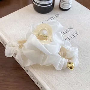 Gros plan d'une pince à cheveux en tissu plissé blanc avec pendentif cœur doré sur livre