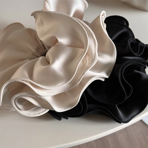 Détail des chouchous en satin champagne et noir avec bords volantés et texture soyeuse